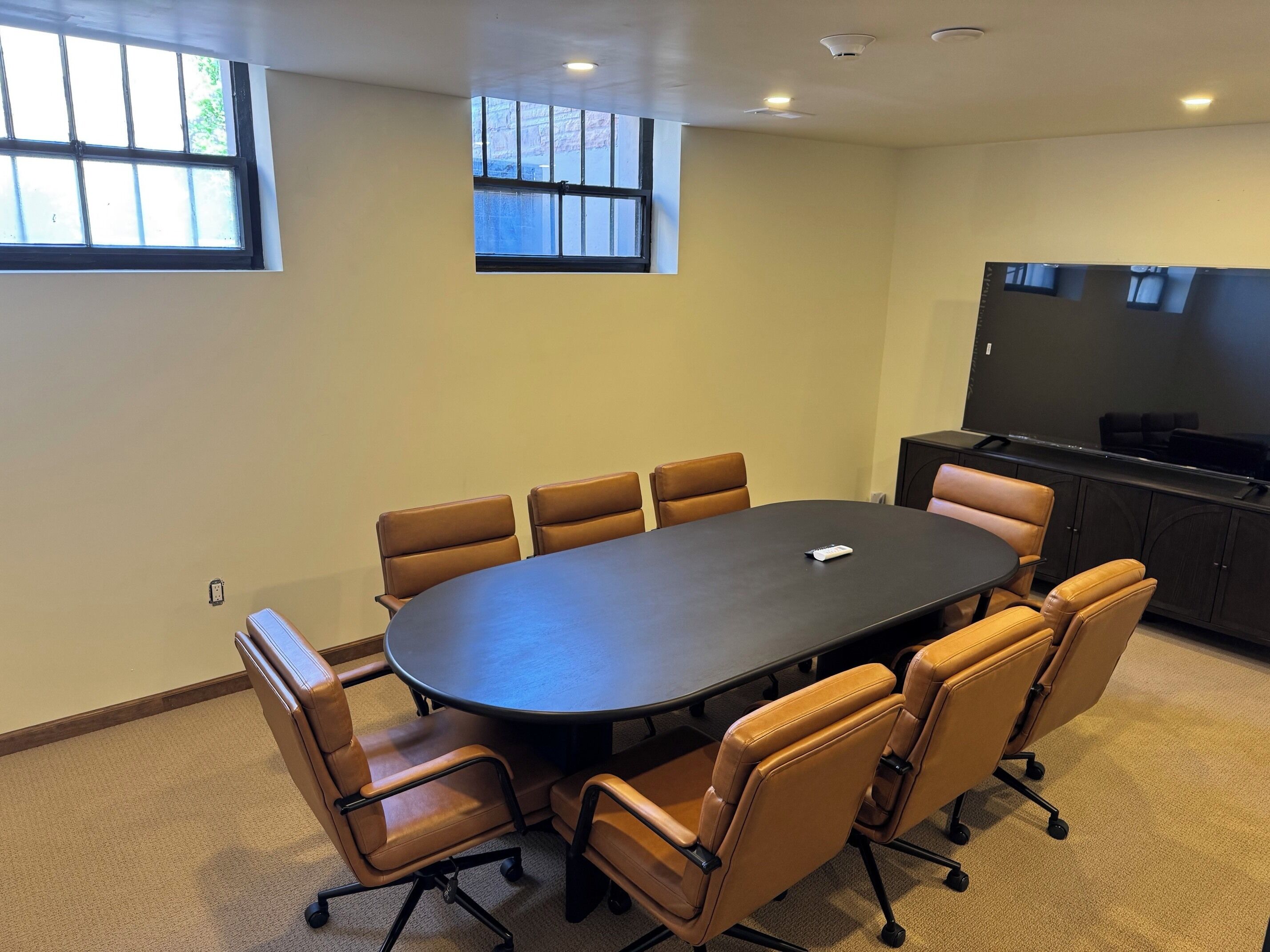 Una sala de conferencias con una gran mesa ovalada, seis sillas, una televisión y una ventana.