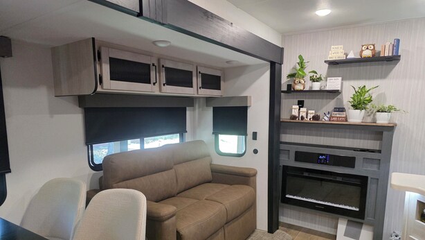 A compact RV interior with a sofa, a dining table, a kitchenette with a stove, and a small shelf with decorative items. - New RV Sleepy Owl ,2-bedroom, 2 bathroom, 1 mile from lake Somerville. (Somerville)