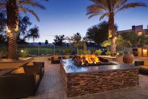 An outdoor patio with a stone fire feature, seating, and palm trees. - Coachella 2027 Rental Available (Palm Desert)