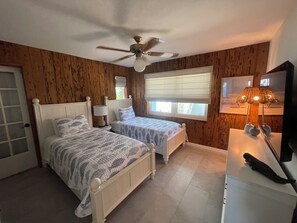Ein Schlafzimmer mit zwei Betten, einem Deckenventilator, einem Fenster mit Jalousien und einer Nachttischlampe.