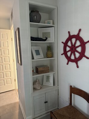 A white storage unit with shelves, a wooden chest, and a ship's wheel decoration on the wall. - Recently Renovated 2bd/2ba a block from the beach & steps from the pool on AMI (Holmes Beach)