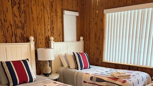 Ein Schlafzimmer mit zwei Betten, einem Deckenventilator, einer Lampe und einem Fenster mit Jalousien.