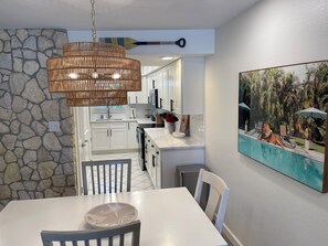 Eine moderne Küche mit weißen Schränken, einer Steinwand und einem Essbereich mit weißem Tisch und Stühlen.