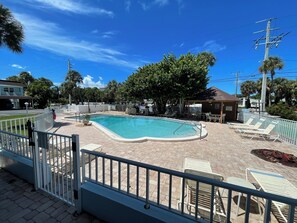 Piscina com deck cercado, cadeiras de descanso e área de estar coberta.