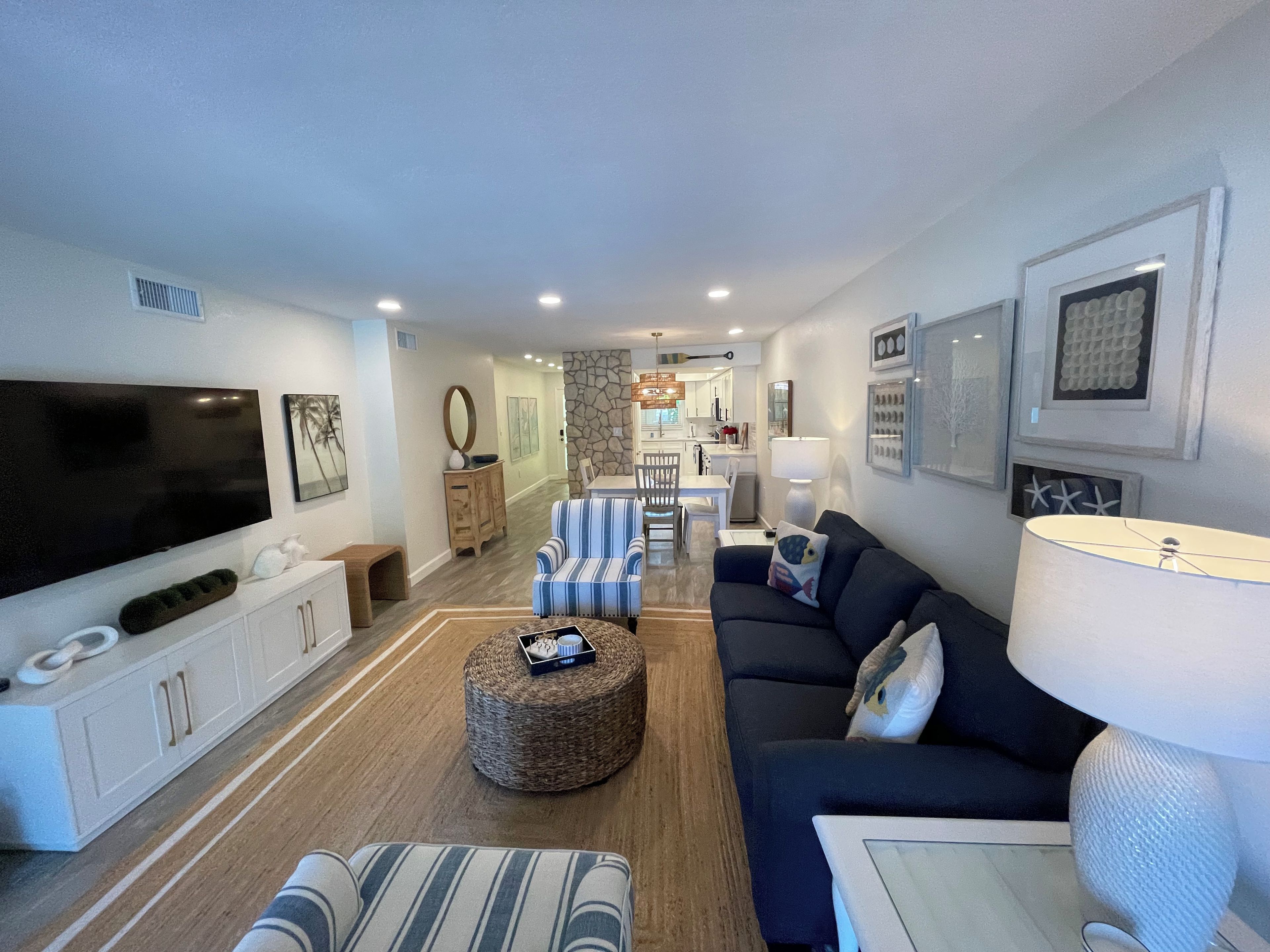 A modern living room with a flat-screen TV, a sofa, a coffee table, and a dining area in the background.