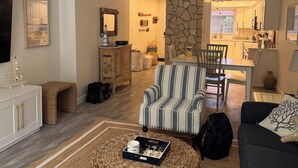 A living room with a TV, a dining area with a table and chairs, and a kitchen in the background. - Recently Renovated 2bd/2ba a block from the beach & steps from the pool on AMI (Holmes Beach)