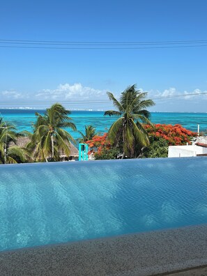 A clear blue pool with a view of the ocean and palm trees. - Oceanview 3-Level Penthouse with Rooftop Terrace and Pool (Isla Mujeres)
