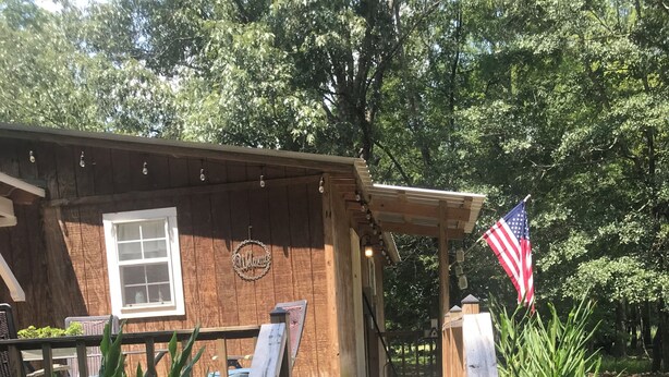 Una cabaña de madera con un porche, un cartel de bienvenida y una bandera estadounidense.