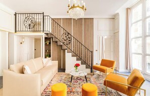 Ein geräumiges Wohnzimmer mit Treppe, einer Chandelüster, einem Sofa und zwei Sesseln.