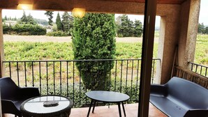 Ein Balkon mit zwei Stühlen und einem Tisch, der auf einen Garten mit Hecke und Weinberg blickt.