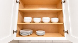 Ein Küchenschrank mit drei Einlegeböden, auf denen Schüsseln und gestapelte Teller stehen.