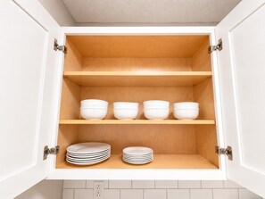 A kitchen cabinet with three shelves, each holding bowls and stacked plates.