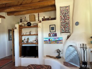 A cozy living room with a fireplace, wooden shelves with decorative items, a television, and a colorful tapestry. - Marveloushouse in charming Ranchos de Taos (Ranchos de Taos)