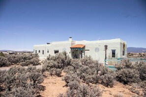 A single-story building with a flat roof, surrounded by sparse desert vegetation. - Marveloushouse in charming Ranchos de Taos (Ranchos de Taos)