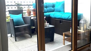Een balkon met rieten meubilair, een bloempot en uitzicht op gebouwen.
