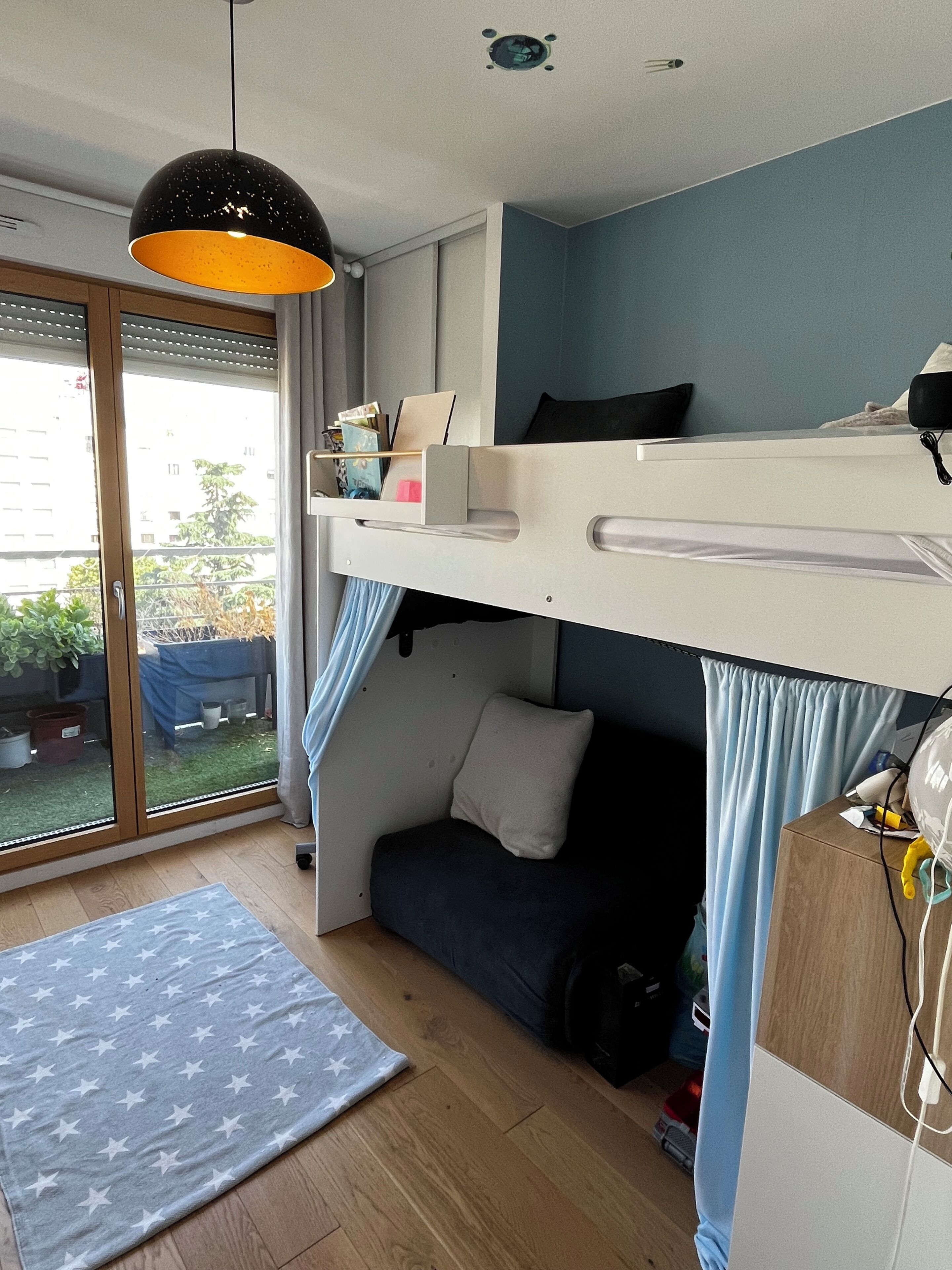 Une chambre avec un lit superposé, un bureau, une lampe suspendue et une vue sur l’extérieur.