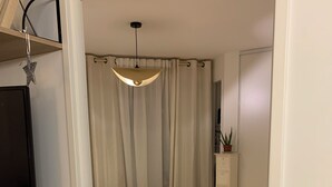 Een slaapkamer met een bed, een dressoir, een televisie op een standaard, een plafondlamp en een deur naar een andere kamer.