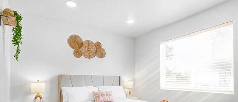 A modern bedroom with a bed, bedside lamps, a decorative wall piece, and a window with blinds.