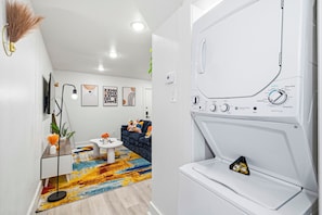 Una sala de estar moderna con un sofá, una mesa de centro y objetos decorativos. Se ve una lavadora al fondo.