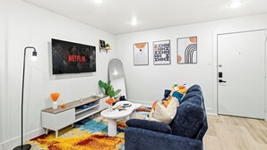 Uma sala de estar moderna com uma televisão de tela plana, um sofá, uma mesa de centro e um tapete colorido.