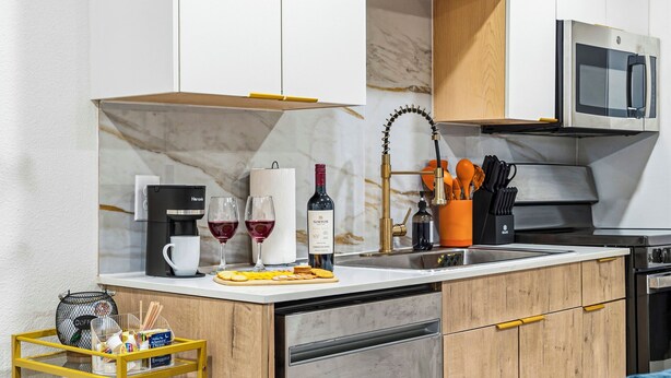 Uma cozinha moderna com micro-ondas embutido, máquina de café, copos de vinho e uma garrafa de vinho no balcão.