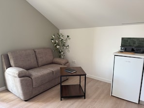 A living room with a sofa, a small table, a refrigerator, and a plant. - Terra Vivaz - Porto Bay Formosa Suite (Porto Formoso)