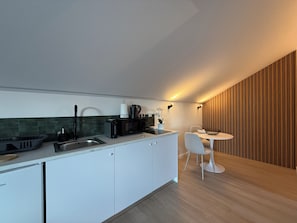 A modern kitchen with white cabinets, a built-in oven, and a dining area with a white table and chairs. - Terra Vivaz - Porto Bay Formosa Suite (Porto Formoso)