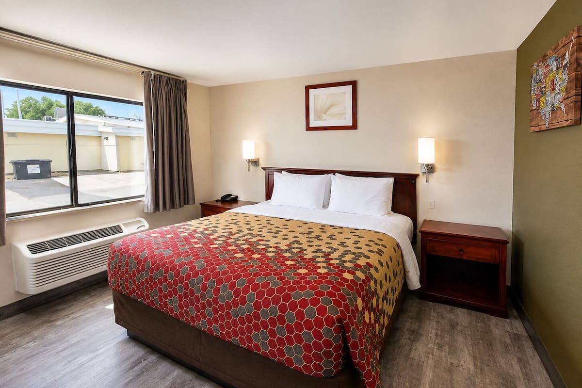 Hotelkamer met een groot bed, twee nachtkastjes, een raam met gordijnen, een aan de muur hangend schilderij en een verwarming.