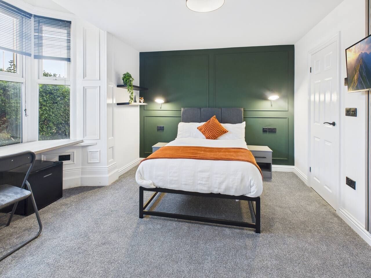 Un dormitorio con cama, mesitas de noche, un escritorio y una ventana.