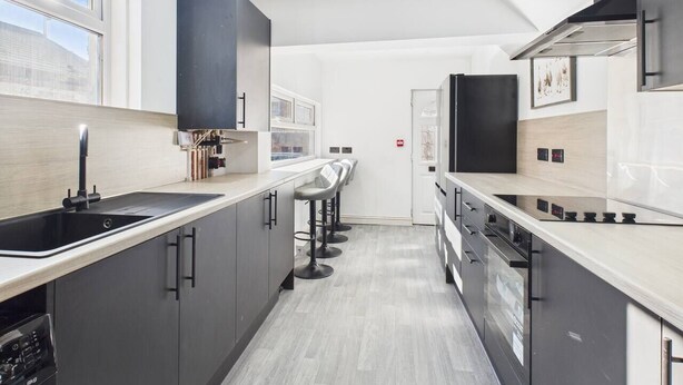 A modern kitchen with a long countertop, black cabinets, and a window providing natural light.