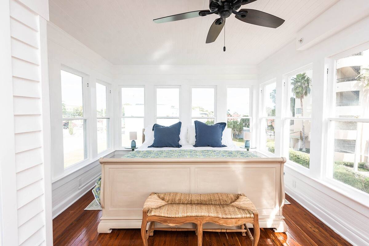 A bright room with a large bed, a ceiling fan, and multiple windows.