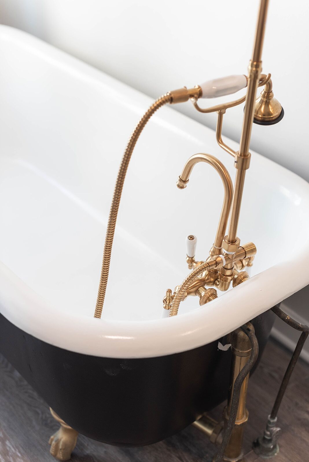 A bathtub with a gold faucet and hose.
