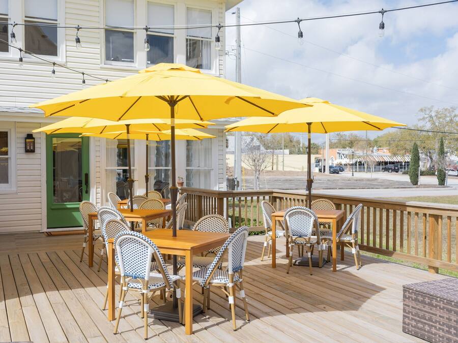 Una terraza de madera con mobiliario exterior, sombrillas amarillas y vista a la calle.