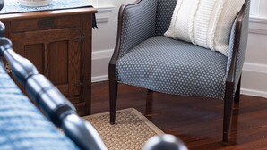Una habitación con un sillón estampado, una mesita de madera con una planta en maceta y una alfombra azul con diseño.
