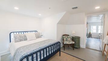 A bedroom with a bed, a chair, a nightstand, and a view of a hallway.