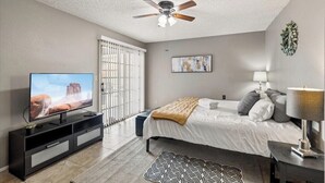 Een slaapkamer met een bed, een televisie, een plafondventilator, een raam met zonwering en een aan de muur hangend kunstwerk.