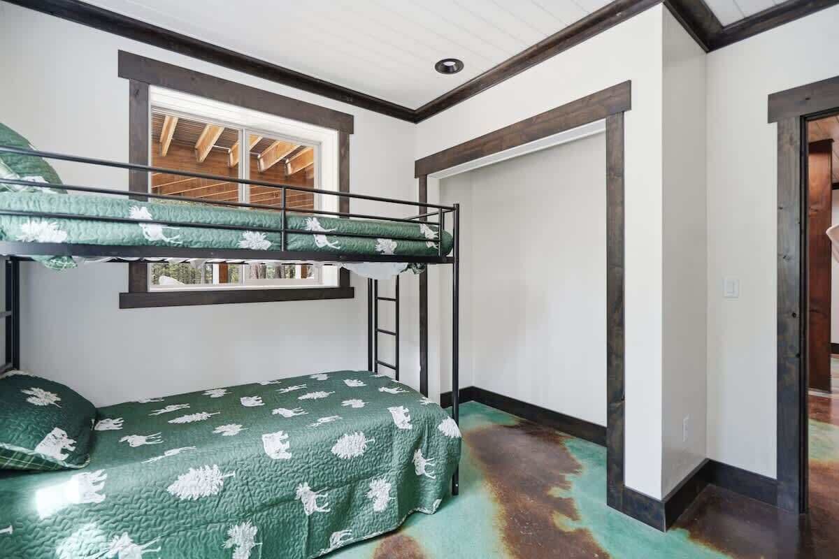 A bunk bed with a ladder, a window, and a door in a room with white walls and a tiled floor.