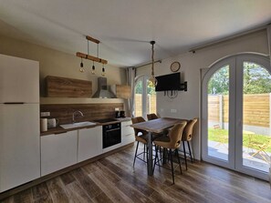 A modern kitchen with wooden cabinets, a built-in oven, and a dining area with a table and chairs. - At Secret des Bois: Air-conditioned house, patio, new appliances. Natural Serenity (Bénifontaine)