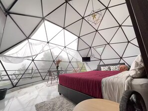 Ein modernes, geometrisches Interieur mit einem Bett, einer Sitzecke und Blick durch ein großes Fenster.