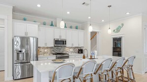 A modern kitchen with white cabinetry, stainless steel appliances, and a central island with bar stools. - Coastal Retreat with Private Pool - Minutes from 30A Beaches (Santa Rosa Beach)
