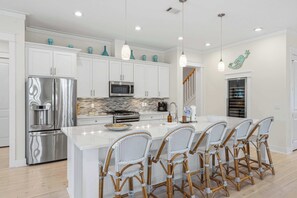 A modern kitchen with white cabinetry, stainless steel appliances, and a central island with bar stools. - Coastal Retreat with Private Pool - Minutes from 30A Beaches (Santa Rosa Beach)