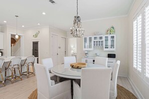 A dining area with a round glass table, white chairs, a chandelier, and white cabinets with glass doors. - Coastal Retreat with Private Pool - Minutes from 30A Beaches (Santa Rosa Beach)