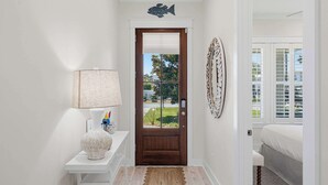 A hallway with a wooden door, a white wall, a lamp, a rug, and a bed in the adjacent room. - Coastal Retreat with Private Pool - Minutes from 30A Beaches (Santa Rosa Beach)