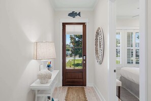 A hallway with a wooden door, a white wall, a lamp, a rug, and a bed in the adjacent room. - Coastal Retreat with Private Pool - Minutes from 30A Beaches (Santa Rosa Beach)