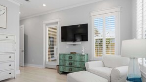 A living room with a white sofa, a teal chest of drawers, a flat-screen TV, and a lamp on a side table. - Coastal Retreat with Private Pool - Minutes from 30A Beaches (Santa Rosa Beach)