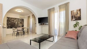 Uma sala de estar com sofá, mesa de centro, televisão e um espaço de jantar com cadeiras.