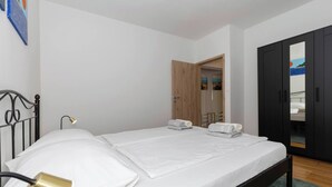Uma cama bem arrumada com lençóis brancos, um abajur e um guarda-roupa preto com espelho.