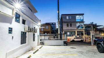Un estacionamiento cerrado con un edificio blanco, una construcción de dos pisos y un SUV estacionado.