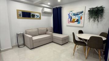 Een moderne woonkamer met een hoekbank, een eettafel met stoelen, een spiegel en een schilderij aan de muur.