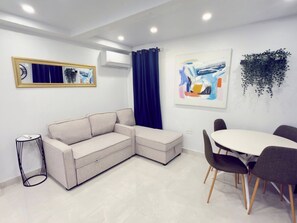 Una sala de estar moderna con un sofá, una mesa de comedor con sillas, una mesita auxiliar y obras de arte en las paredes.